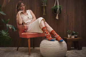 woman sitting on an orange chair wearing a beige dress and colorful mushroom patterned organic socks