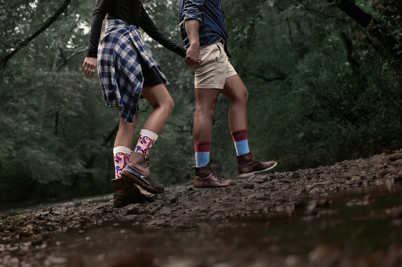 man and woman holding hands walking on a river bank wearing boots and patterned organic cotton socks