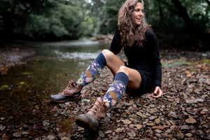 woman sitting on a river bank wearing knee high, flower patterned organic cotton socks