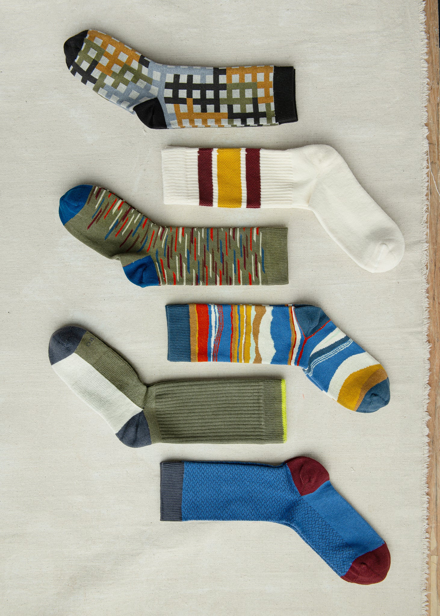 men's organic cotton socks in various styles, colors and patterns laying on a tan surface