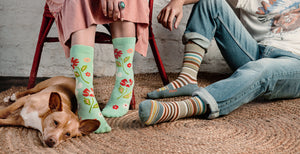 woman and man sitting down wearing brightly colored organic cotton socks. Cute dog at the feet of the woman.